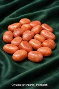 Buy crystals for chakras online shown as red aventurine stones on dark green cloth.